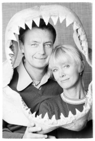 Black and white  Portrait shot of Ron and Valerie Taylor framed by a shark jaw Ron is holding up