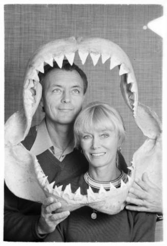Black and white  Portrait shot of Ron and Valerie Taylor framed by a shark jaw Ron is holding up