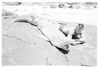 Black and white  Shot of person laying alongside a caught shark on a beach shoreline