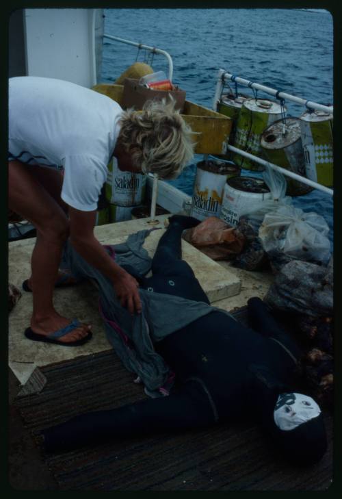 Mark Heighes bent over holding mesh suit on test dummy lying on a wharf