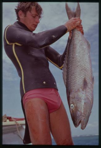 Shot of person in wetsuit top holding a caught fish by the tail