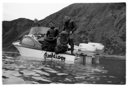 Shot of two divers on 'Reefdiver' dinghy holding fish nets near a shoreline at sea