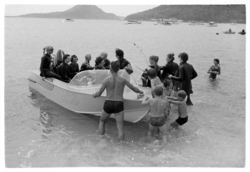 Shot of group of adults and children pushing dinghy with passengers in knee-deep water