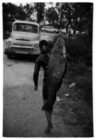 Shot of diver holding large caught fish over their back walking along a road