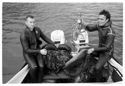 Shot of two divers holding their fishing catch and crayfish on board at sea