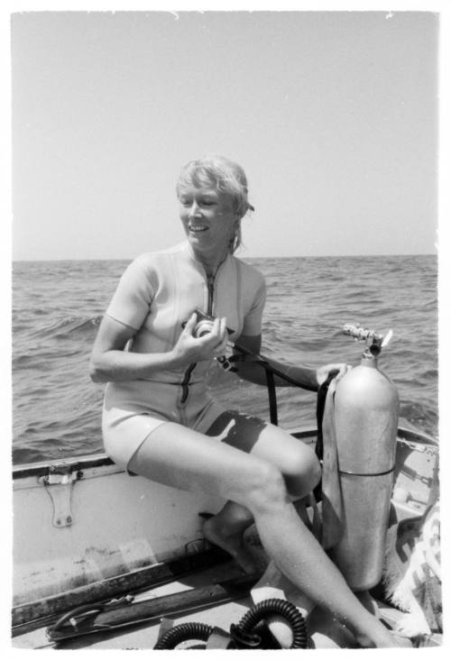 Shot of Valerie Taylor holding camera sitting on board the back of a boat by a air cannister