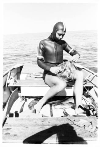 Topside shot of diver sitting at back of dinghy at sea holding underwater camera gear