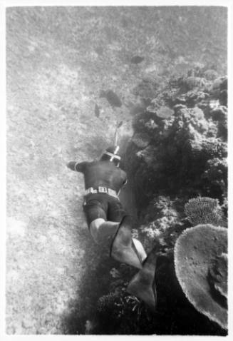 Underwater shot looking down on a freediver swimming towards sandy seafloor with sparse scattered coral