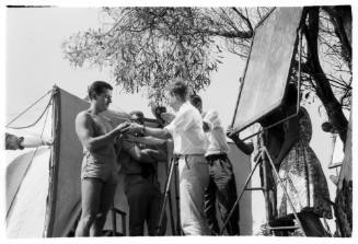 Shot of group of people with array of filming equipment standing on land infront of a large pitched tent