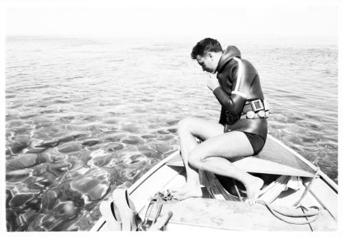 Topside shot of diver sitting at back of dinghy at sea looking down at adjacent water