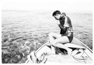 Topside shot of diver sitting at back of dinghy at sea looking down at adjacent water