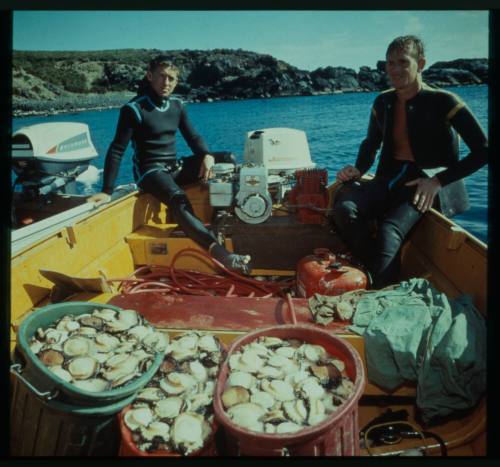 Shot of two people in dive gear sitting with three barrels of shellfish on a dinghy at sea