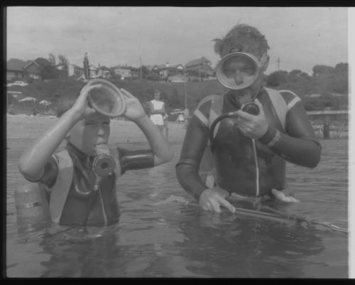 Black and white shot of adult and child standing in chest-deep water in scuba diving gear