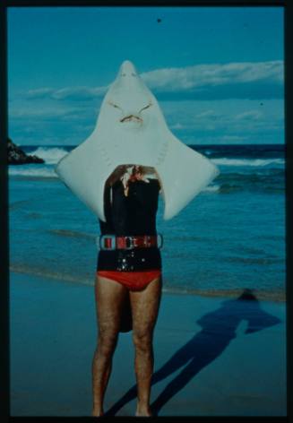 Shot of person holding head of a Skate (fish) with only pectoral fins attached, standing at the water's edge at a beach