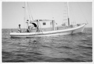 Black and white shot of a yacht (Riversong) on calm sea with two people at stern with no sails up