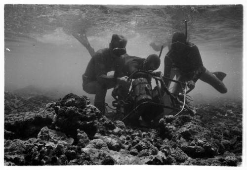 Black and white underwater shot at rocky floor in shallow water of divers moving equipment