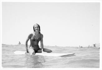 Black and white shot at water surface of person sitting on surfboard at sea