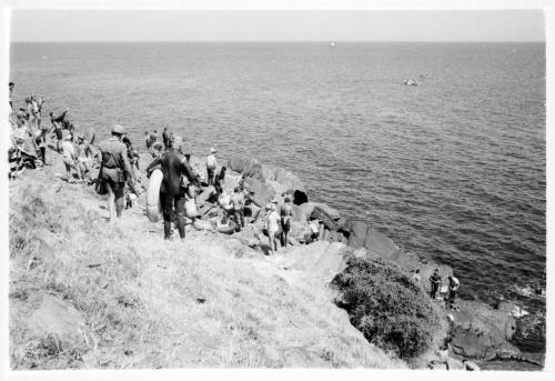 Black and white shot of group of divers on grassy coastline with sea in background