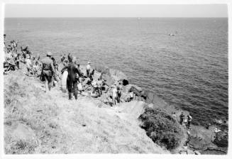 Black and white shot of group of divers on grassy coastline with sea in background