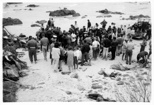 Black and white shot of large crowd standing in ankle deep water on rocky platform and outcrops