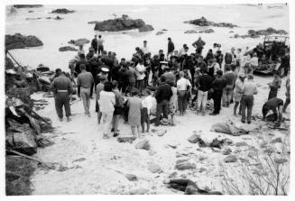 Black and white shot of large crowd standing in ankle deep water on rocky platform and outcrops