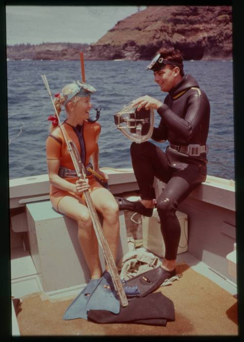 Shot of Valerie Taylor with spear rod and Ron Taylor with underwater film equipment both suited in dive gear