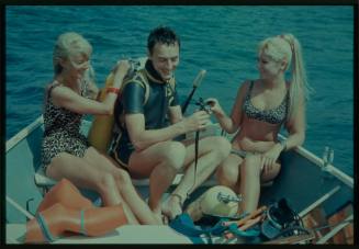 Shot of Valerie Taylor, Ron Taylor and third person amongst dive gear sitting on board a boat at sea