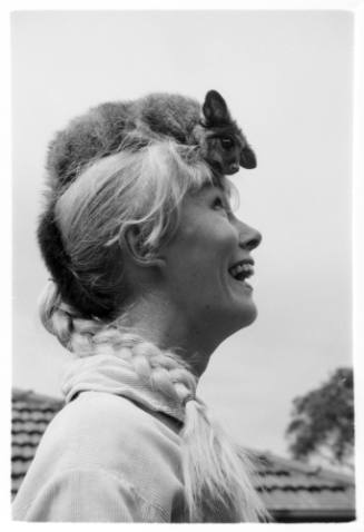 Black and white close up side portrait of Valerie Taylor with possum on her head