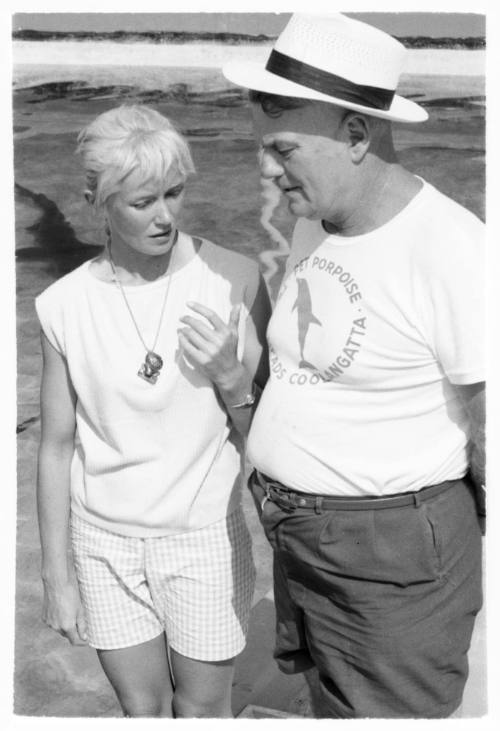 Black and white shot of Valerie Taylor with Jack Evans standing on the beach shoreline of Porpoise Pool