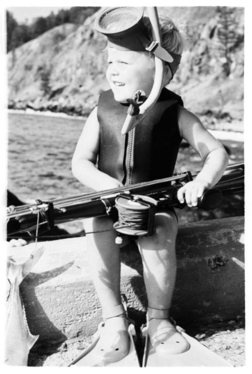 Black and white shot of child in dive gear sitting holding a fishing rod on lap