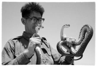 Black and white shot of person holding a live snake in each hand