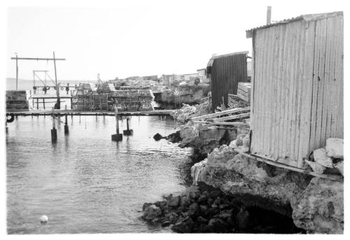 Black and white shot of a wharf and rocky shoreline with small metal sheds along the edge