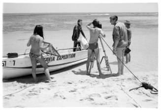 Black and white shot of group of people at waters edge alongside a dinghy, with some handling film equipment