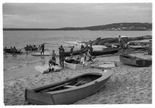 Black and white shot of beach shore with group of people and group of dinghies ashore