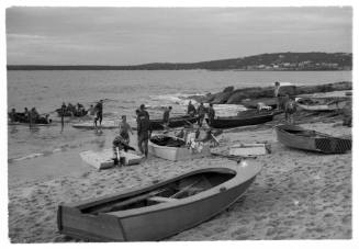 Black and white shot of beach shore with group of people and group of dinghies ashore