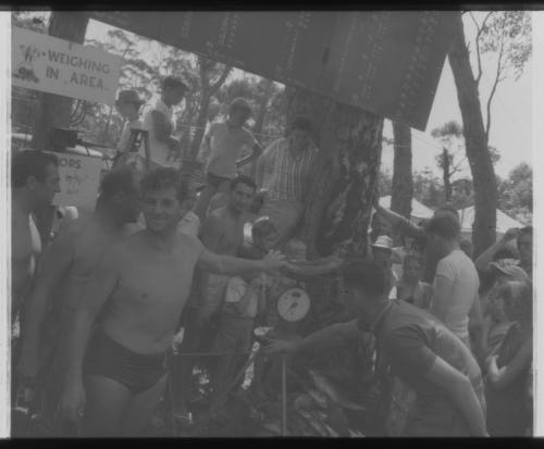 Shot of person standing by his fish being weighed at a weighing area amongst crowd