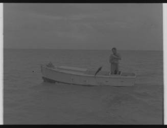 Shot of person fishing alone on board a dinghy pulling in a caught fish at sea
