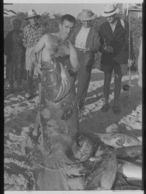 Shot of person holding a large caught fish standing amongst their catch on the floor at the beach