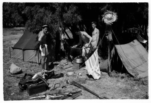 Black and white shot of campsite with four people and multiple pitched tents