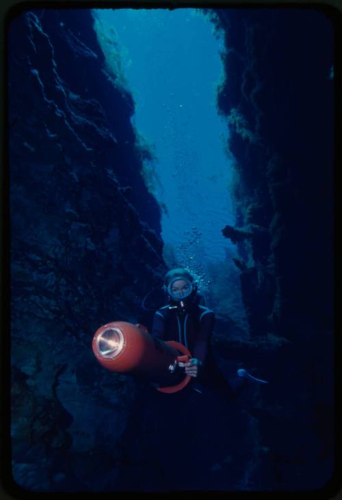 Valerie Taylor underwater swimming through a crevice