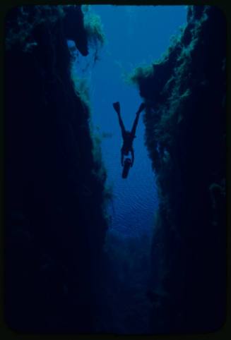 Silhouette of diver underwater swimming through crevice