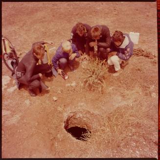 Five people looking at a hole in ground