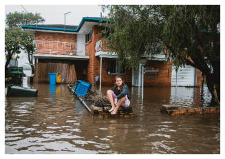 Person seated on brick fence surrounded by flood water