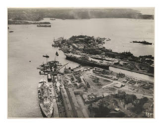 Aerial view of a King George V class battleship and two Royal Navy aircraft carriers at Garden Island Naval Dockyard, Sydney Harbour