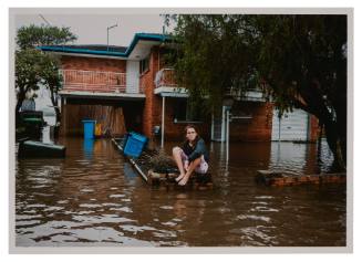 Person seated on brick fence surrounded by flood water