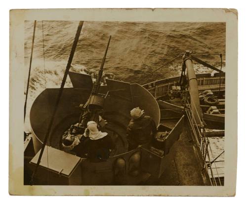 Close-up view of three crew members attending to ship's gun on board vessel