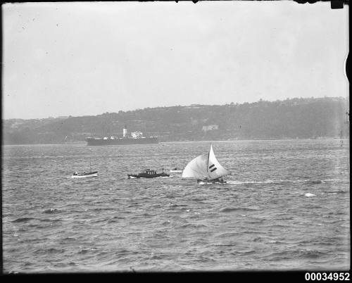 Sailing boat in harbour with motor launch and cargo boat in background.