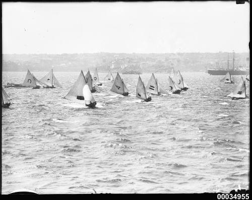 Racing regatta showing 16 boats with full sails in harbour.