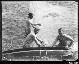 Image of three men in water with a capsized yacht