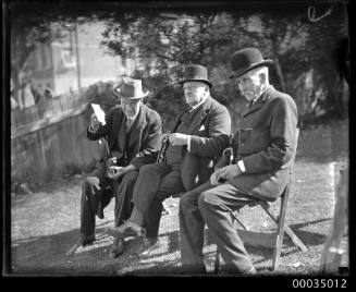 Three men, including Judge Alfred Paxton Backhouse, wearing suits and hats seated on a lawn